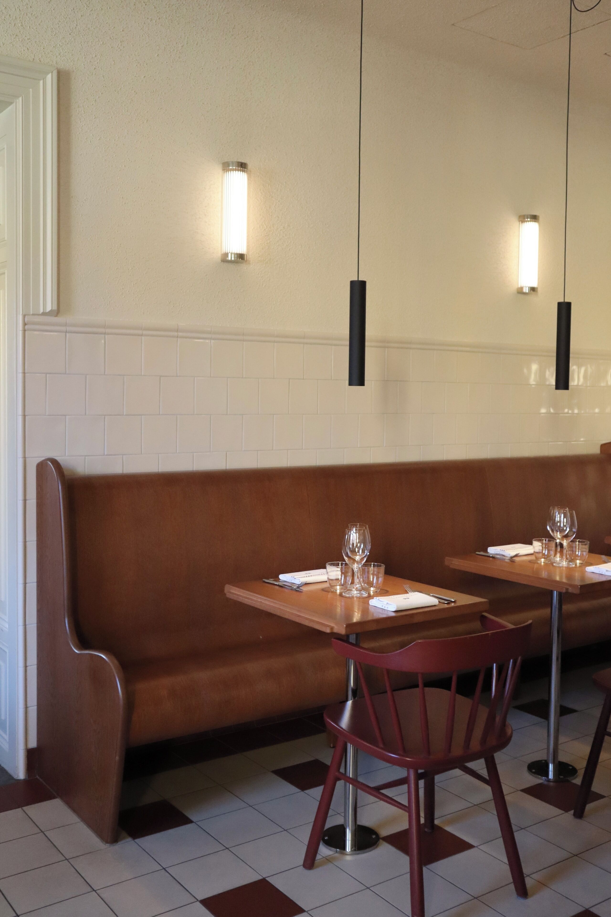 A restaurant interior with a wooden bench, tables, chairs, and pendant lighting.