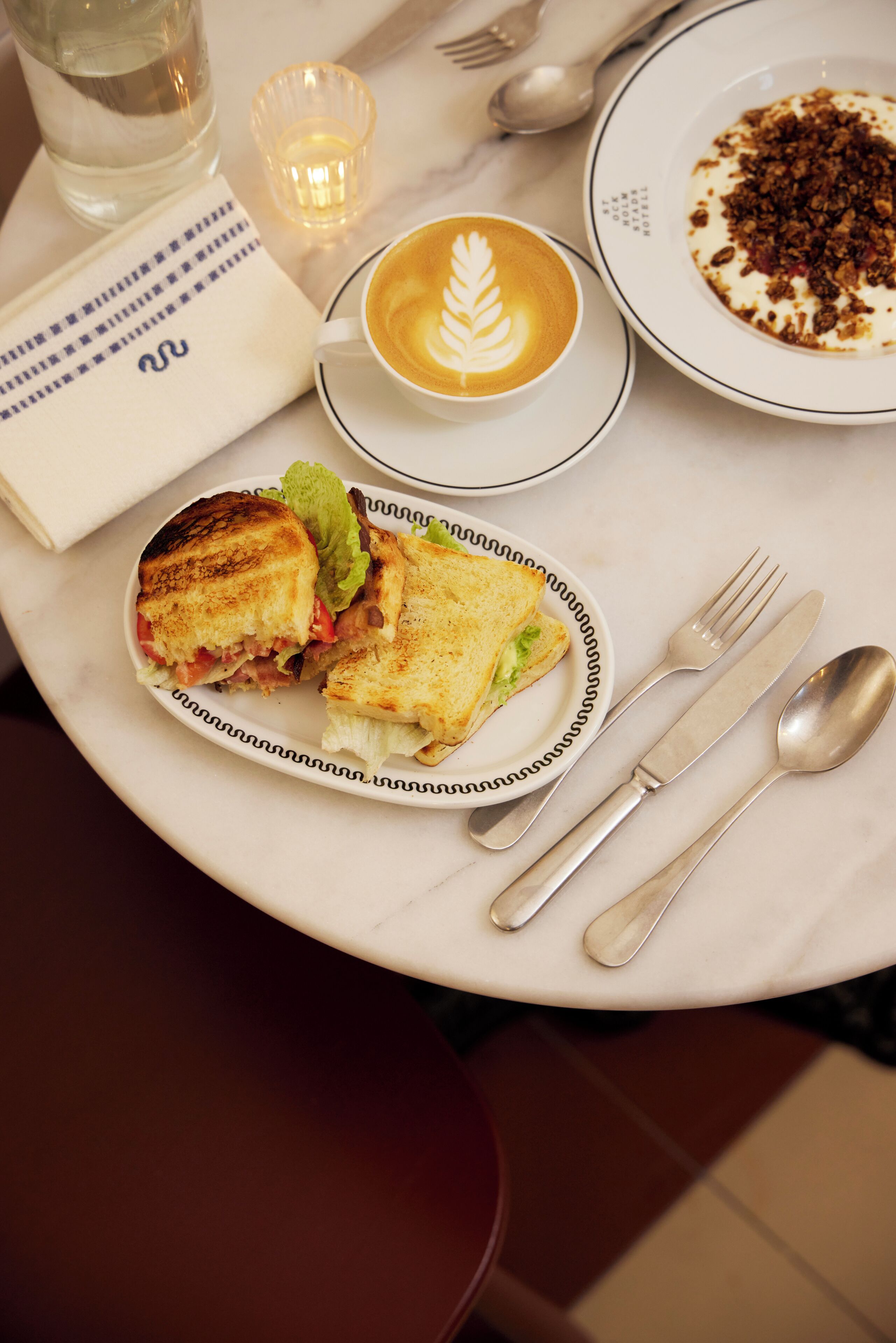 A table with a sandwich, a cup of coffee, and a plate with food remnants.