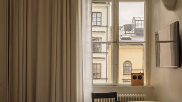 Une chambre d’hôtel avec une grande fenêtre, un lit, une chaise, une petite table et un radiateur.