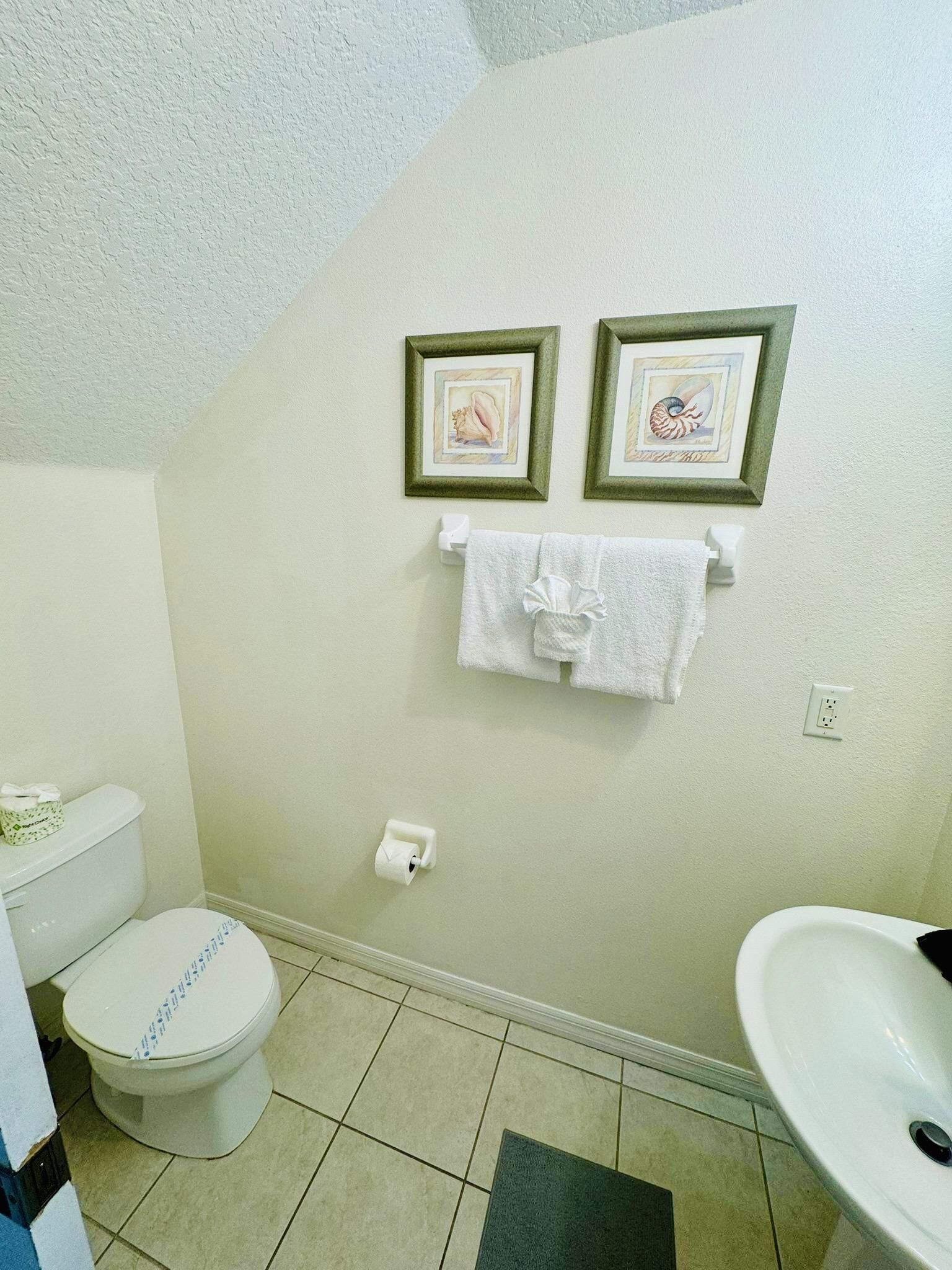 Ein Badezimmer mit Toilette, Waschbecken und zwei gerahmten Bildern an der Wand.