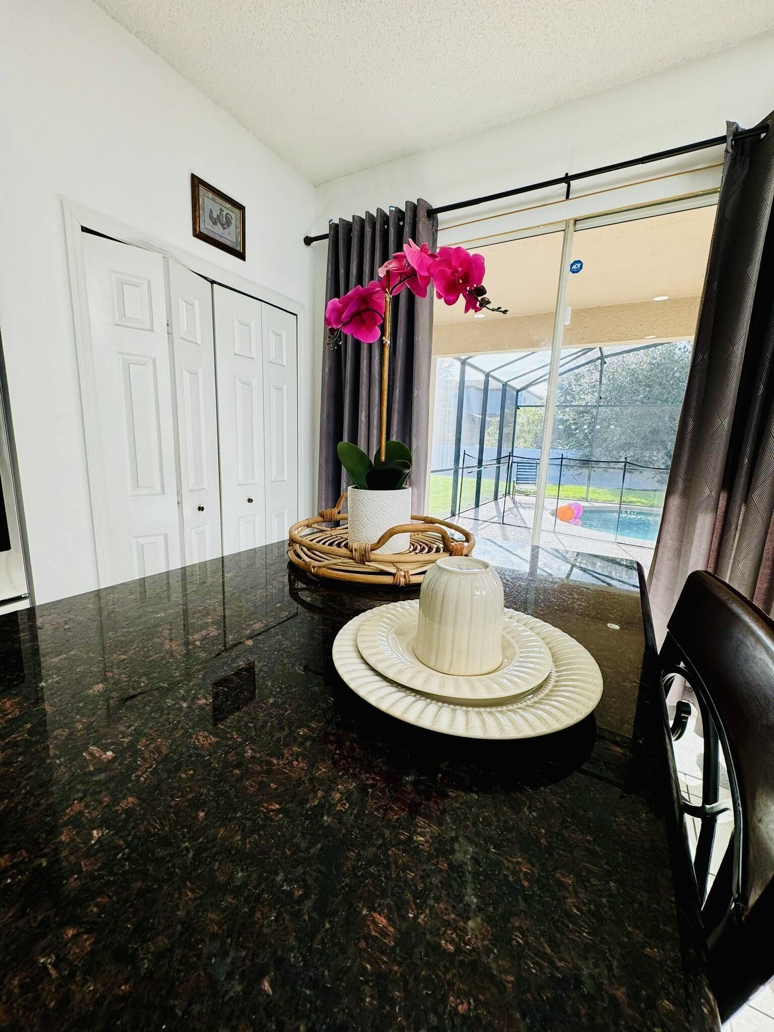 Un coin repas avec une table en marbre noir, un vase blanc et une chaise en osier.