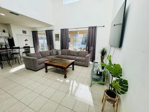 A spacious living room with a sectional sofa, a wooden coffee table, and a TV mounted on the wall. - 7/6.5 Beautiful Vacation Home With Private Pool, and Much More!! (Kissimmee)