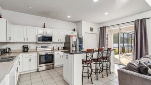 Une cuisine moderne avec des meubles blancs, un îlot central doté de tabourets, un réfrigérateur et un four.