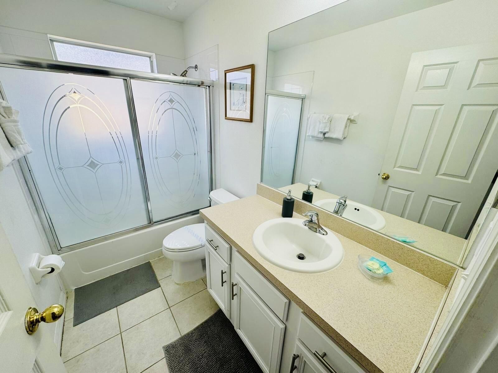 Une salle de bain moderne avec une douche à parois de verre, des toilettes blanches, un lavabo avec un miroir et une porte dotée d’une poignée en laiton.