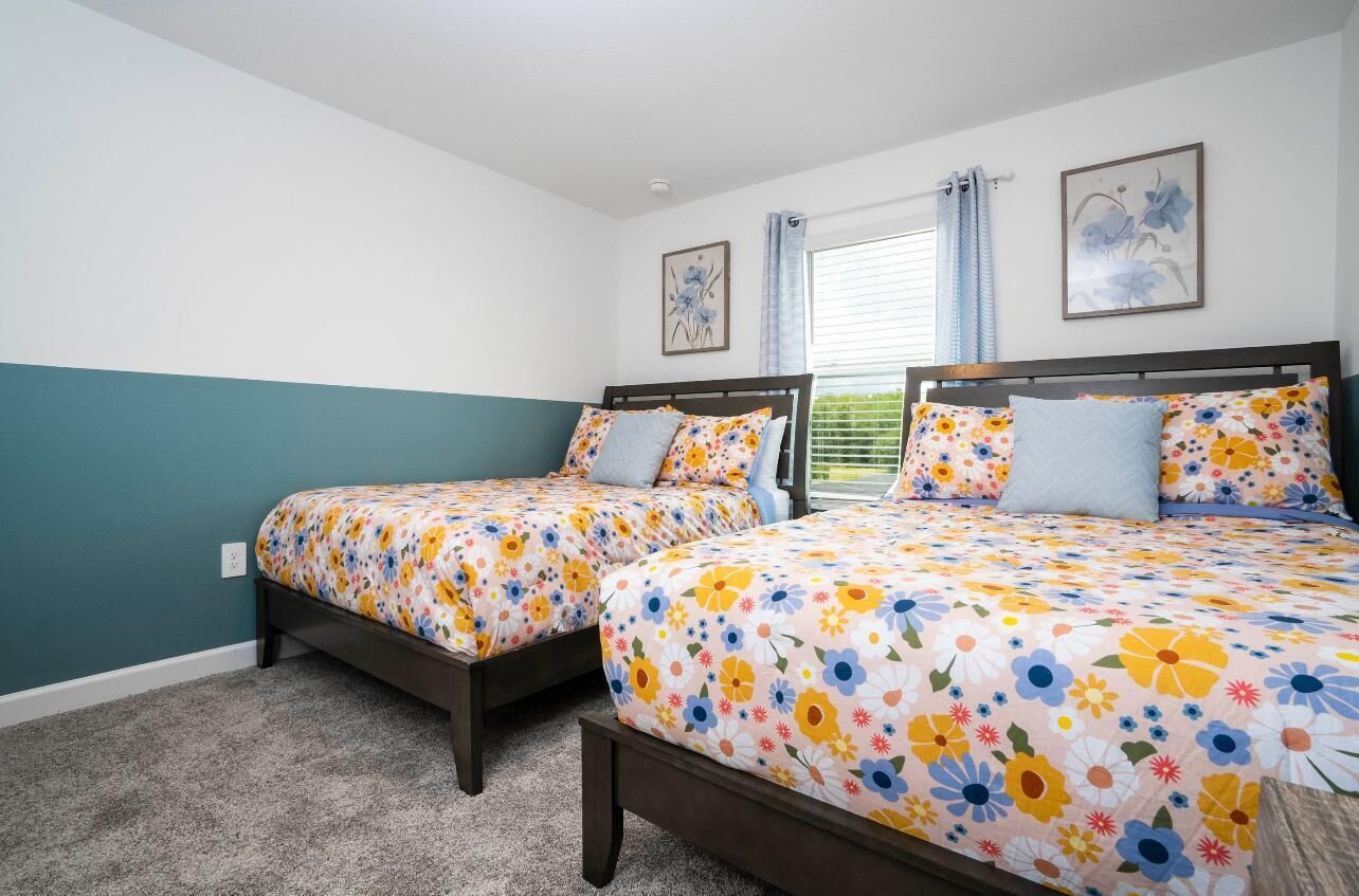Une chambre avec deux lits, une literie à motifs floraux, une fenêtre avec des rideaux et des œuvres d’art accrochées aux murs.