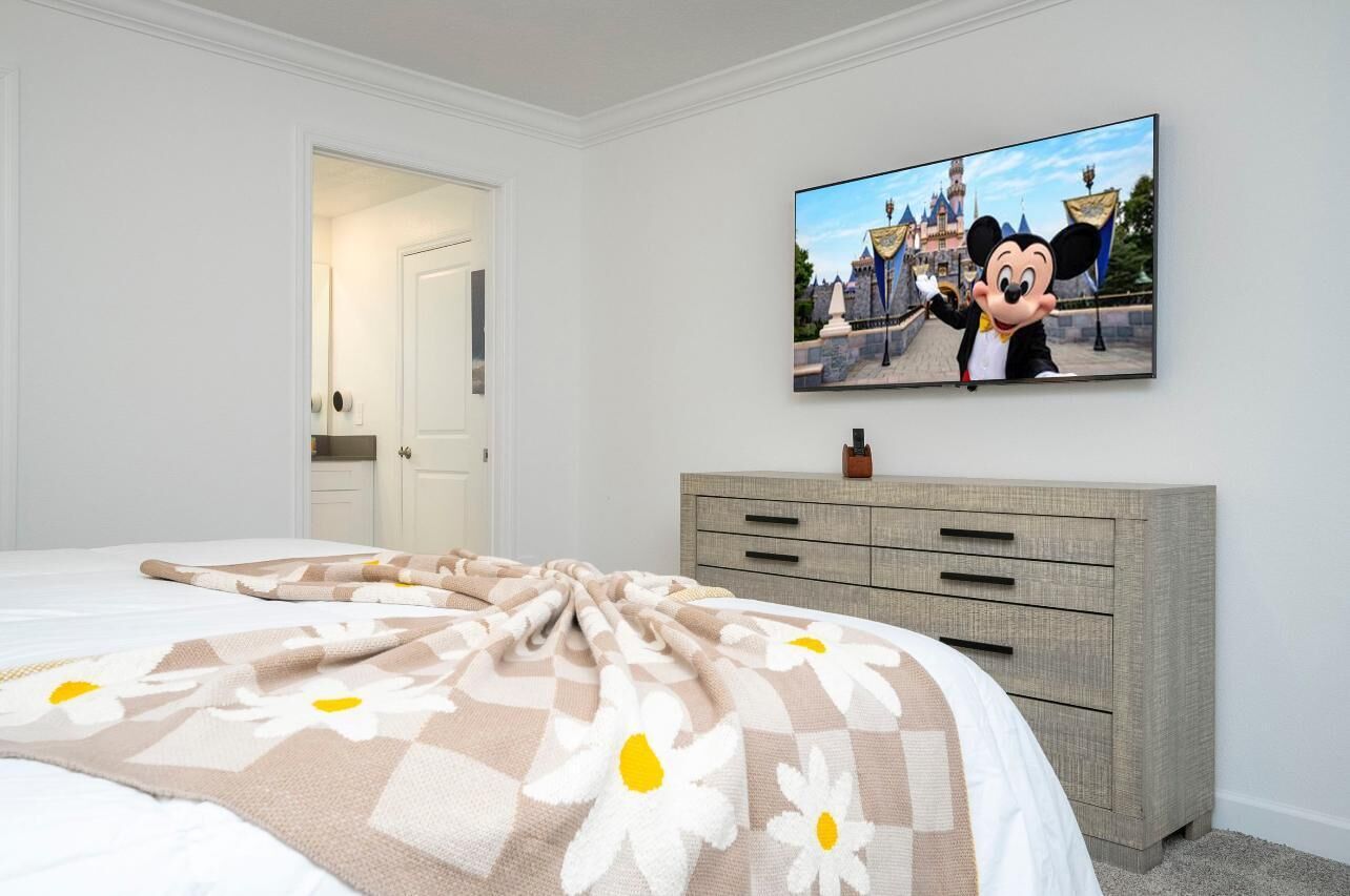 Et soveværelse med en seng, et fjernsyn der viser Mickey Mouse, og en kommode.