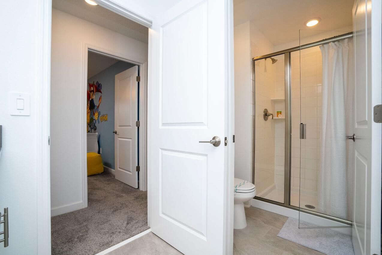 A bathroom with a glass shower enclosure, a toilet, and a white door.