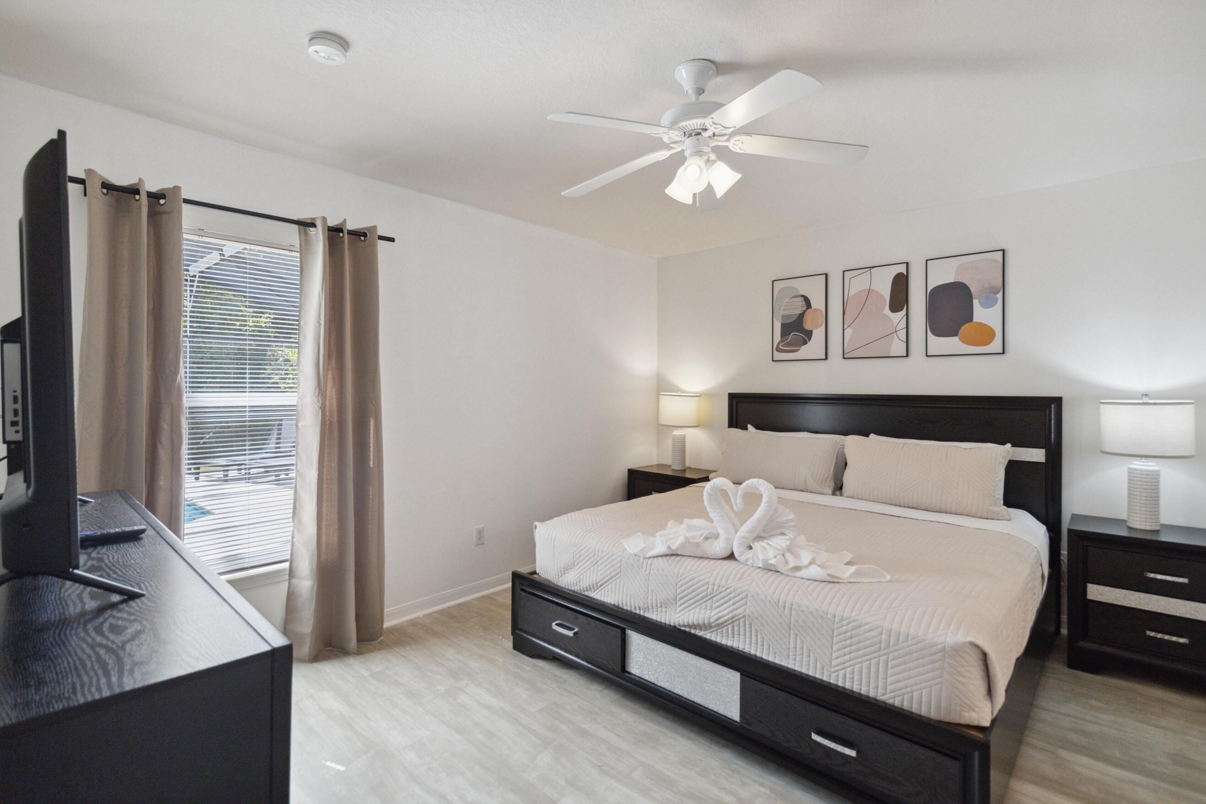 A bedroom with a bed, a ceiling fan, a desk, and a TV.