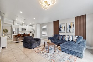 Un soggiorno moderno con divano, poltrone, tavolino da caffè e una cucina sullo sfondo.