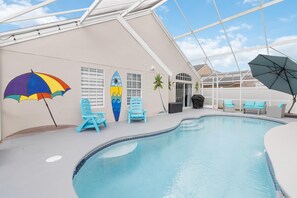 Una piscina interna con soffitto in vetro, poltrone da relax blu, un murale con una tavola da surf e un ombrellone colorato.