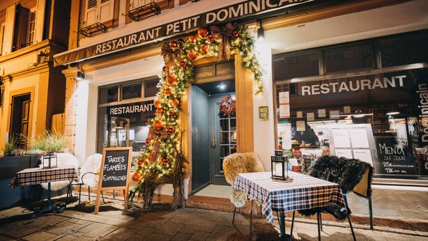 Een restaurant genaamd 'RESTAURANT PETIT DOMINICAIN' met terras en feestelijke kerstversiering.