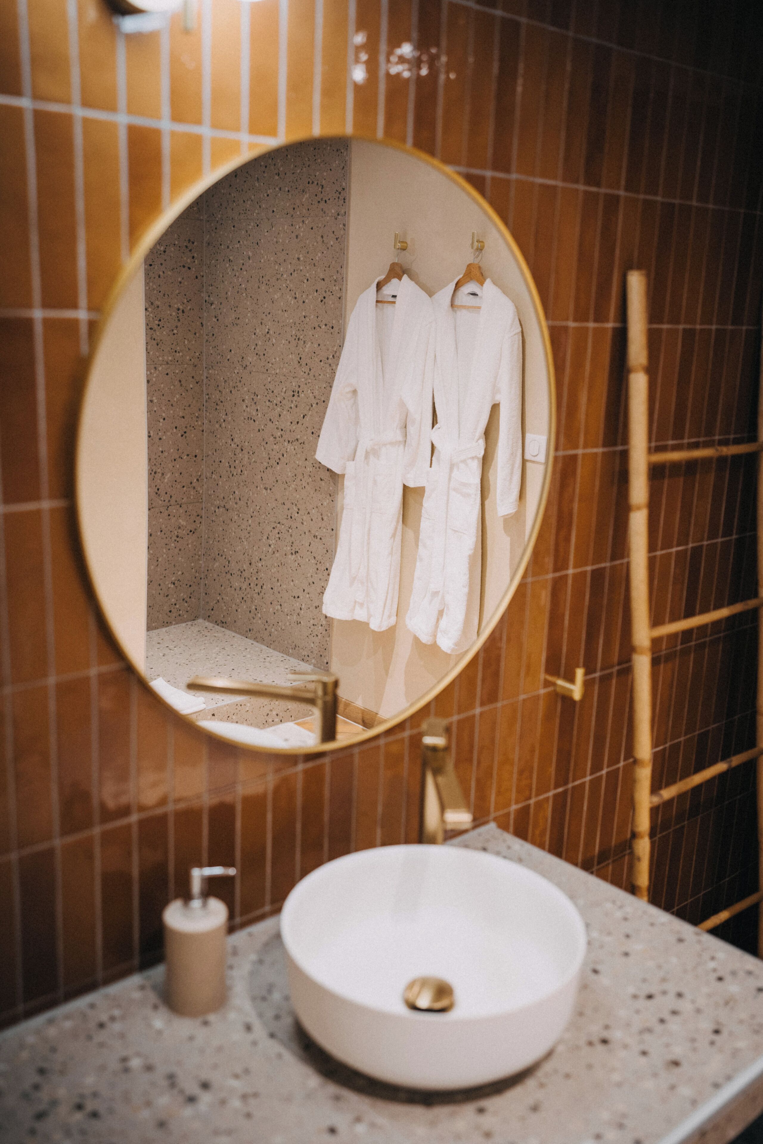 Ein Badezimmer mit rundem Spiegel, Waschbecken und zwei weißen Bademänteln, die auf einem Gestell hängen.