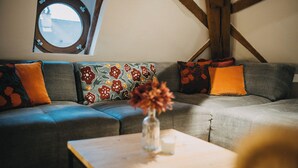 Een moderne woonkamer met een hoekbank, decoratieve kussens, een vaas met bloemen en een bijzettafeltje.