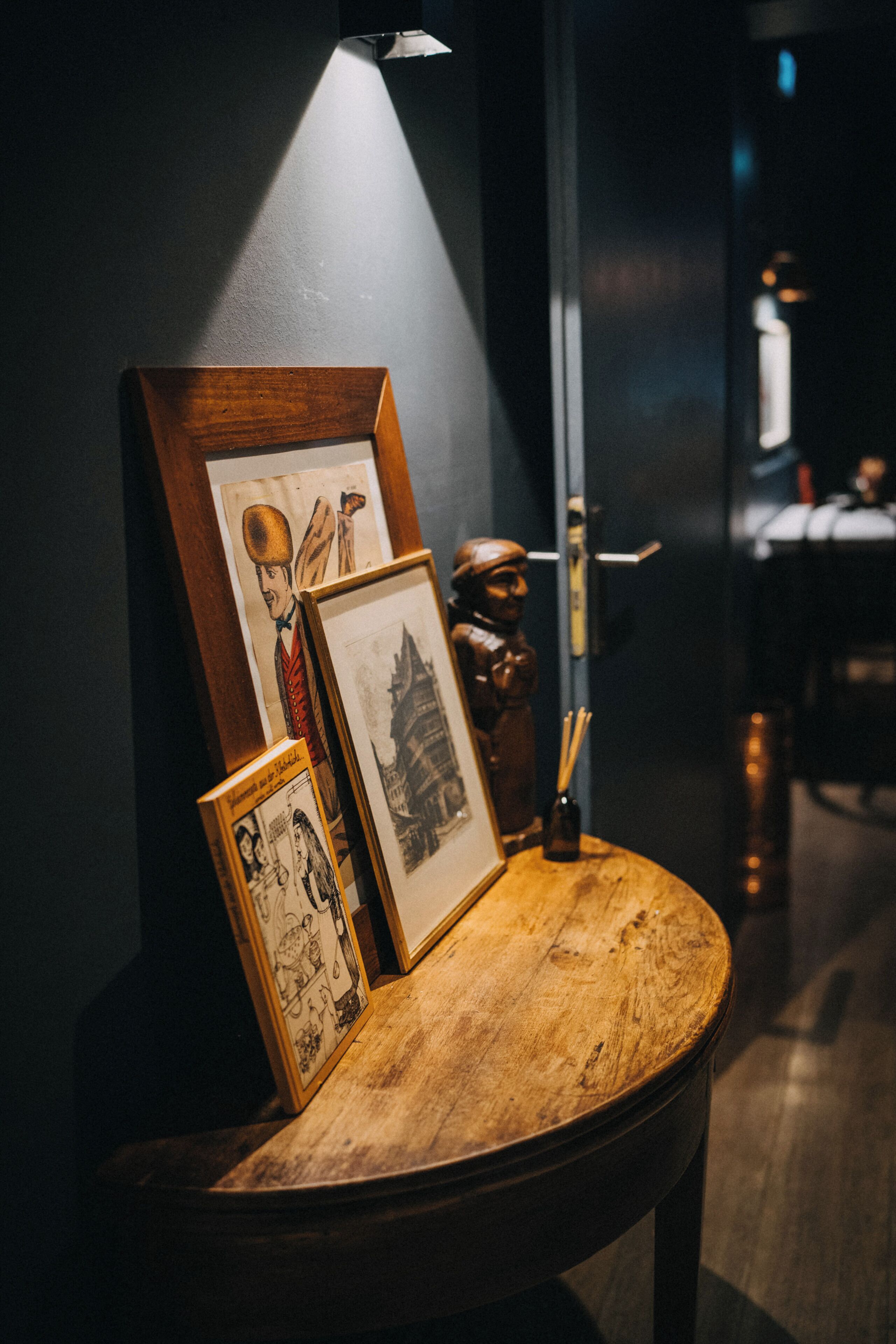 A wooden table with framed artwork and a small figurine, illuminated by a spotlight.