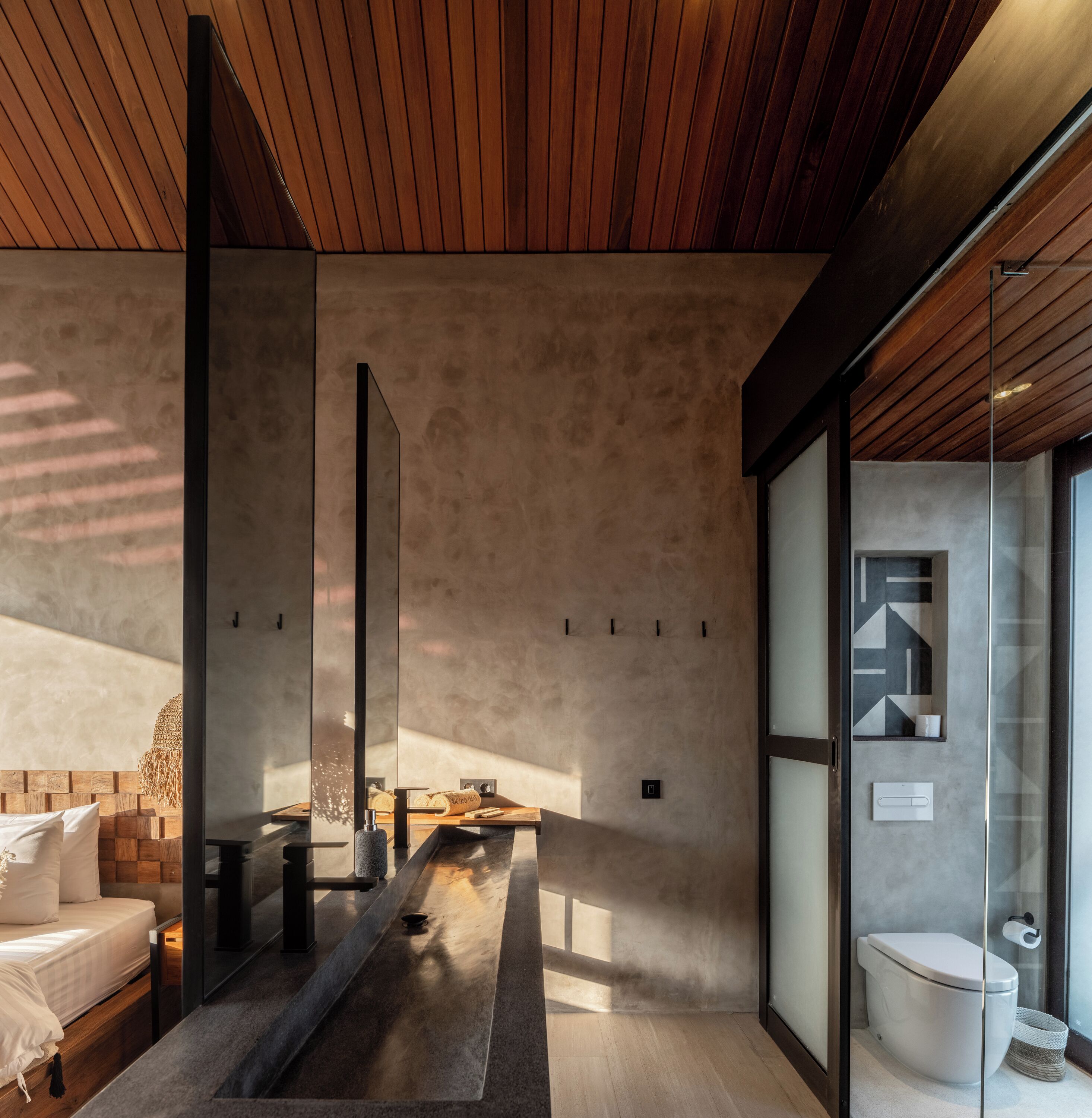 Un baño moderno con diseño minimalista, que cuenta con techo de madera, cabina de ducha de vidrio y un inodoro a la vista.