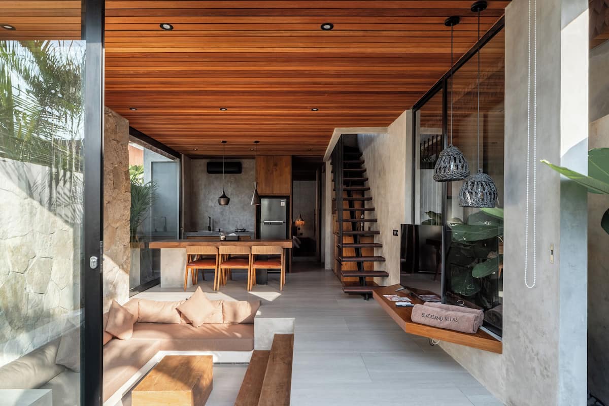 Een modern interieur met een houten plafond, een keuken met een centraal eiland, een trap en een zithoek met een bank en salontafel.