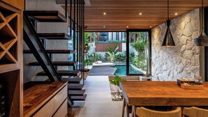 Un interior moderno con una escalera de madera, un comedor con vistas a una piscina y un jardín, y una pared de piedra.