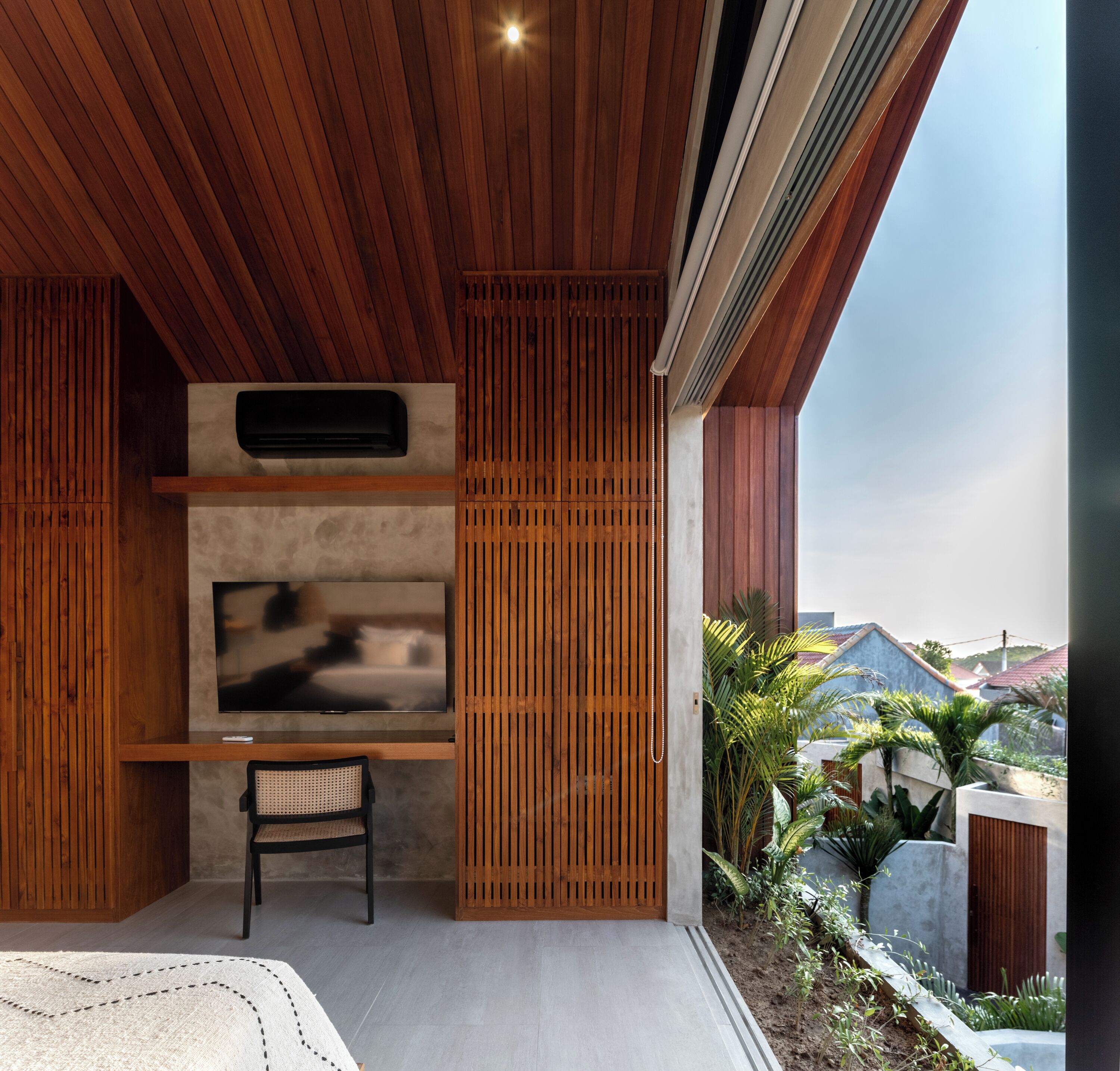 A modern living room with a flat-screen TV, wooden paneling, a bench, and a view of the outdoors.