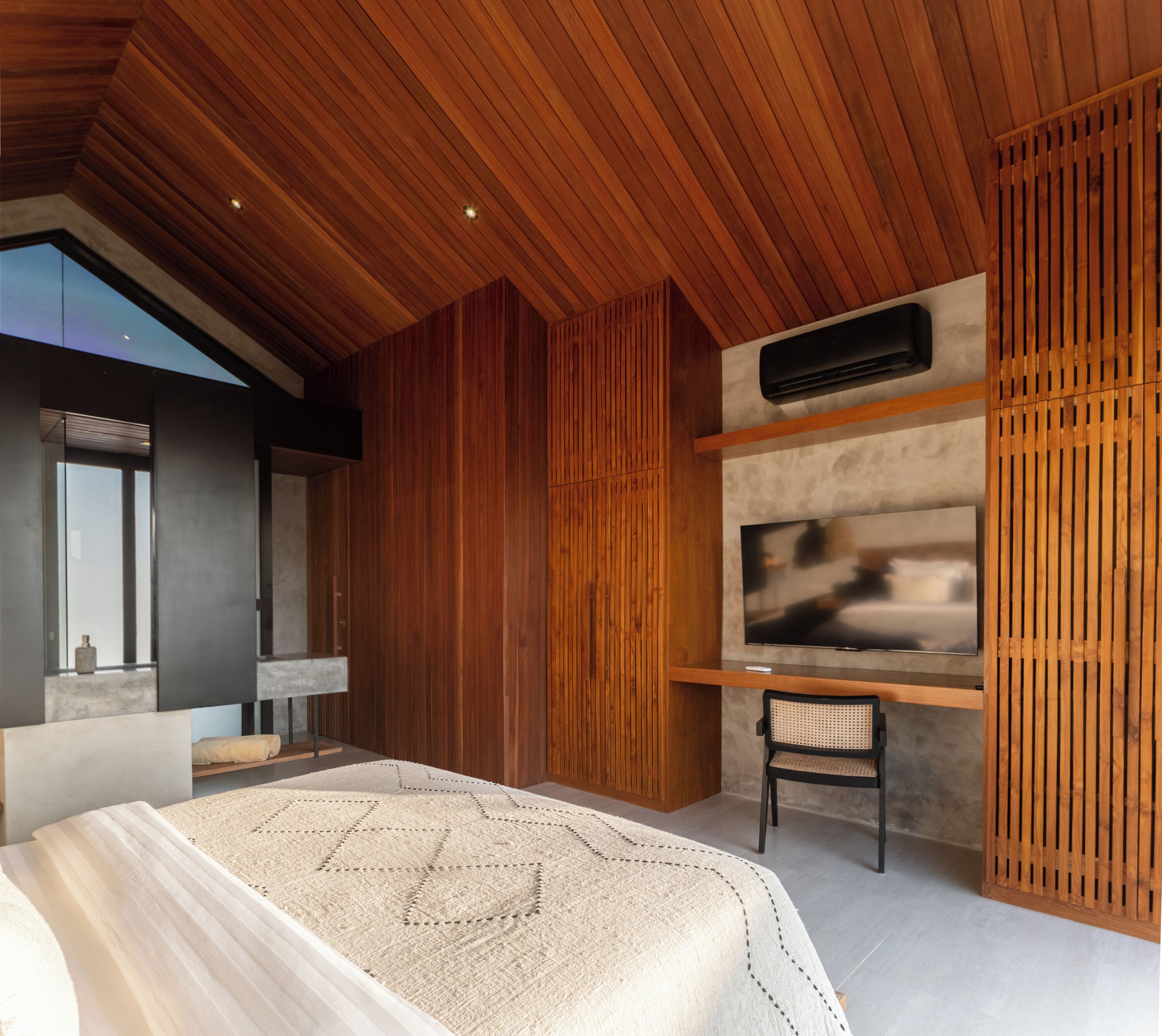 A modern bedroom with a large bed, a TV mounted on a wooden wall, and a desk with a chair.