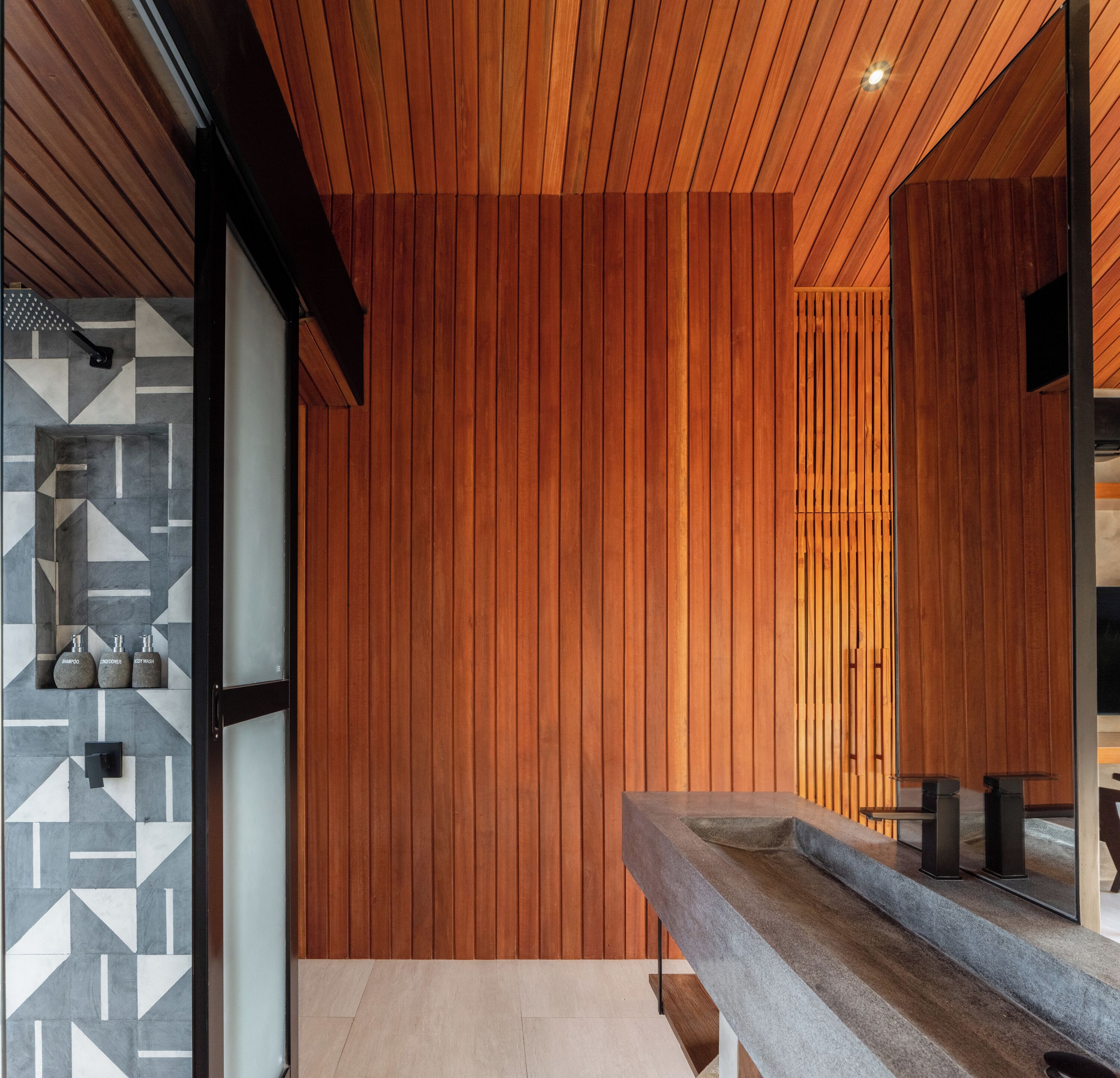 Un baño moderno con paneles de madera, un lavabo de piedra y un salpicadero de azulejos geométricos.