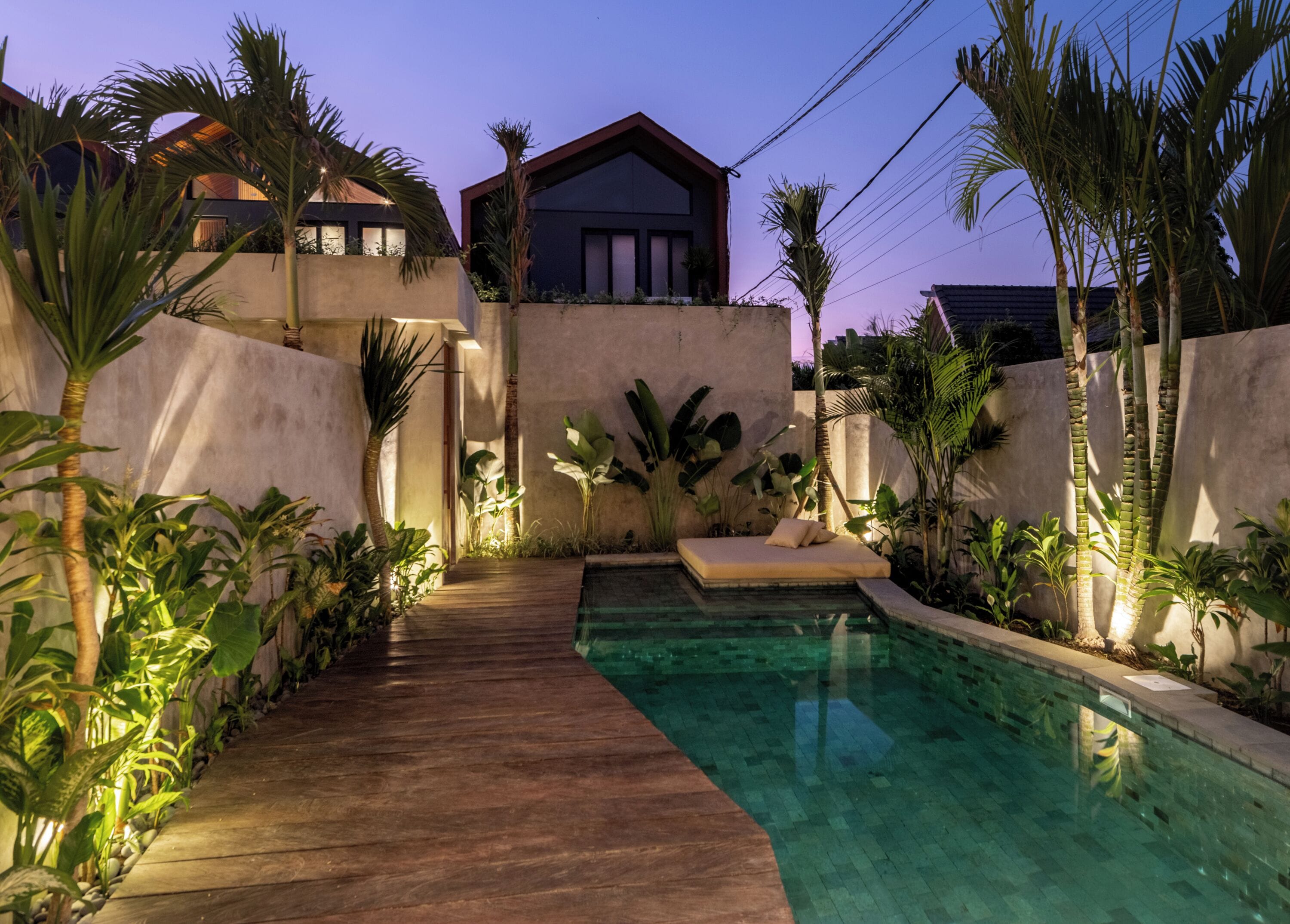 Area piscina con un pavimento in legno, una sedia a sdraio e piante tropicali.