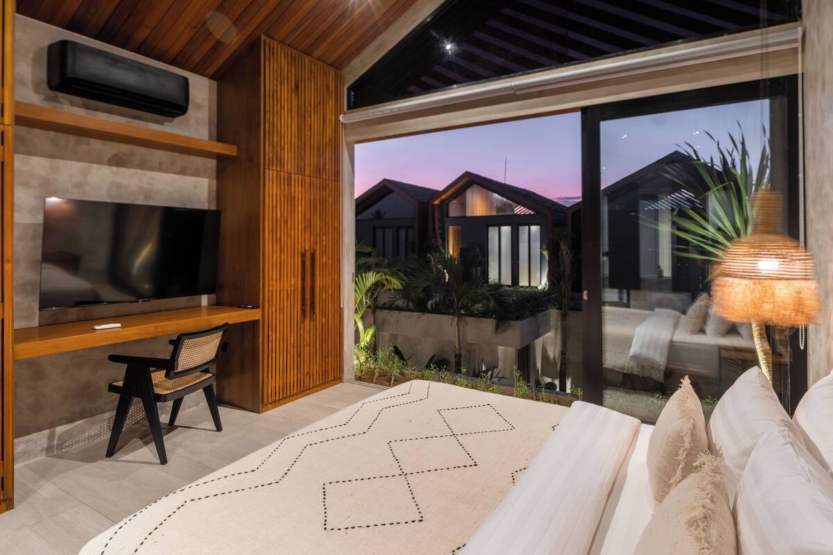 Een moderne woonkamer met een televisie, houten plafond en een groot raam met uitzicht op een tuin.