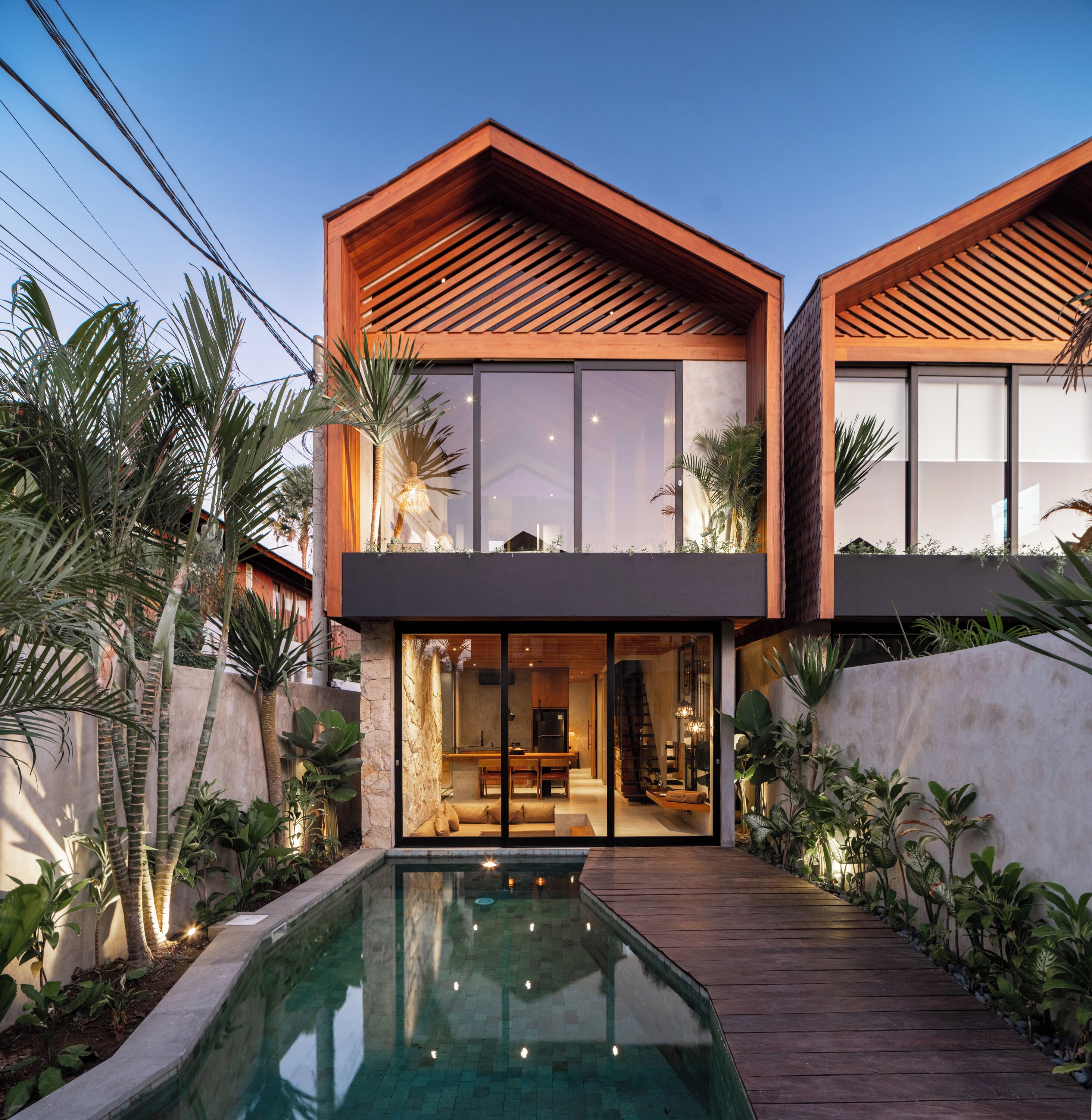Una casa moderna de dos pisos con piscina, ventanas amplias y terraza de madera.