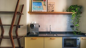 Uma cozinha com cafeteira, pia, micro-ondas e uma estante com obras de arte e uma planta.