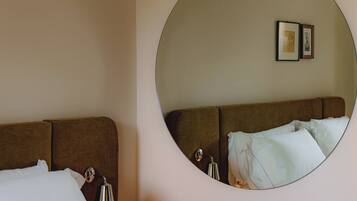 Quarto de hotel com cama, um espelho redondo na parede e uma mesa de cabeceira com luminária.