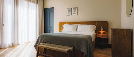 A bedroom with a bed, a bench, a nightstand, a wooden cabinet, and a door.