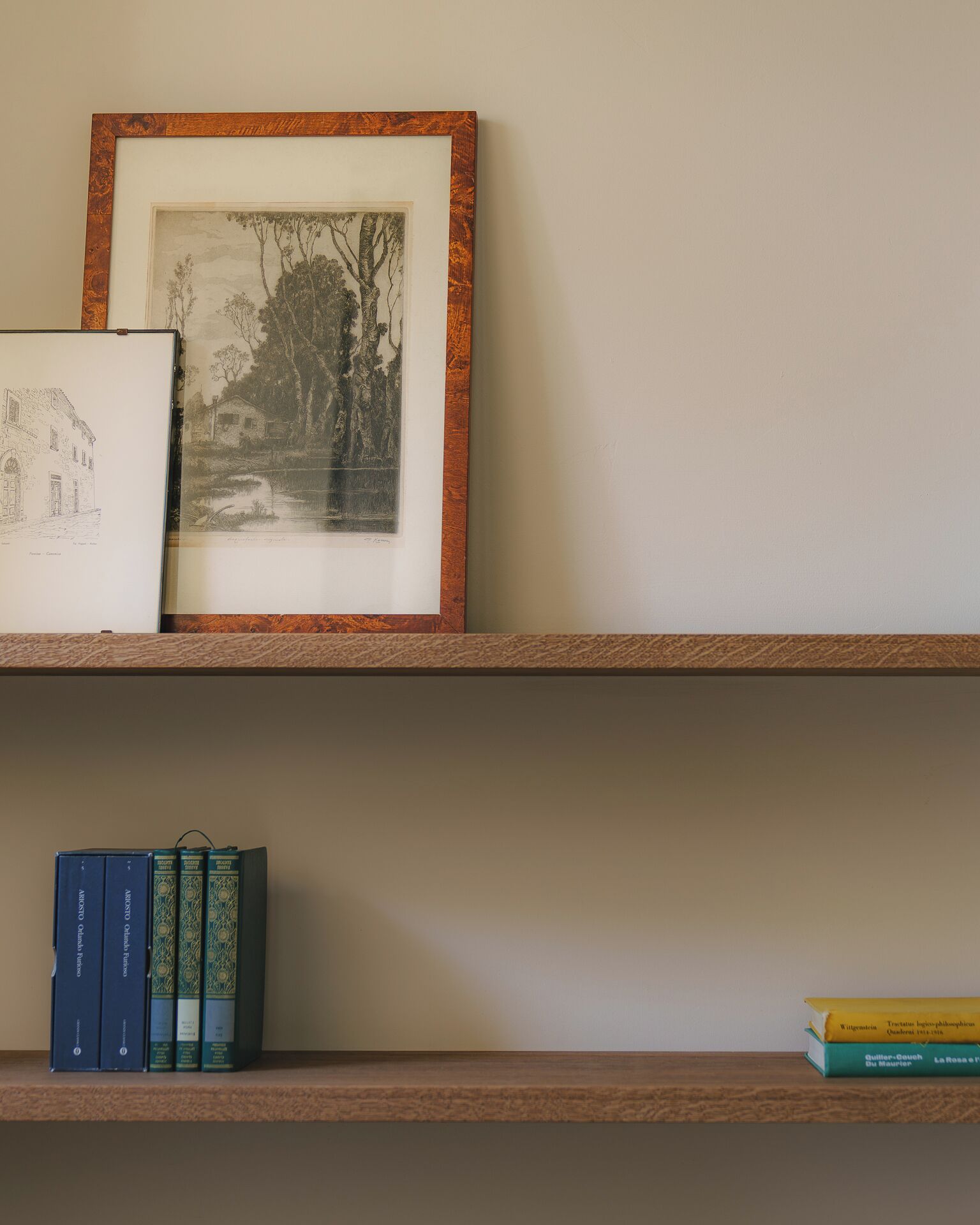 A bookshelf with a framed etching and three books.