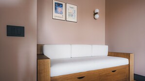 Quarto moderno e minimalista com sofá em estilo banco de madeira, duas obras de arte emolduradas na parede e luminária fixada na parede.