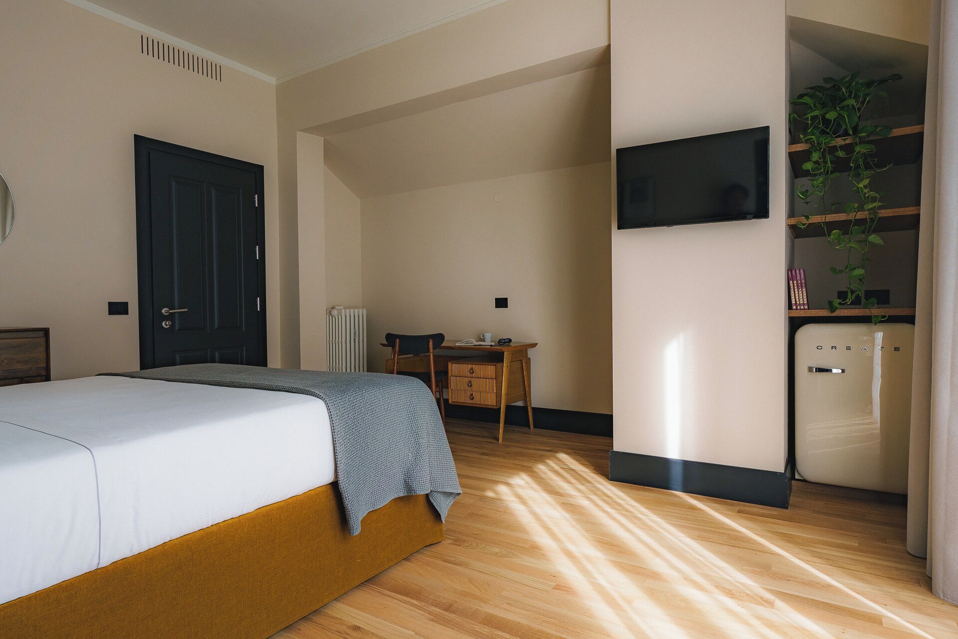 A bedroom with a bed, a desk, a chair, a radiator, a television, and a refrigerator.