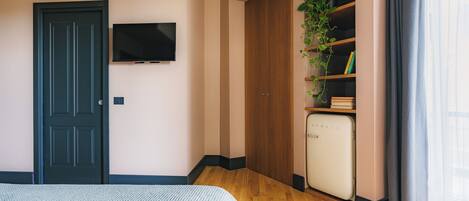 Une chambre avec un lit, une télévision, une armoire, un petit réfrigérateur et une plante.