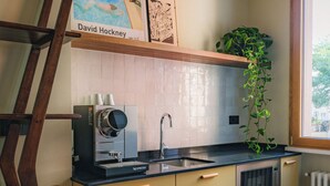 Cozinha com escada de madeira, máquina Nespresso, pia e janela com planta.