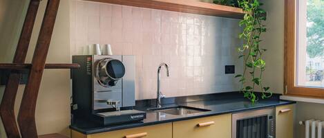 Una cocina con una escalera de madera, una máquina Nespresso, un lavamanos y una ventana con una planta.