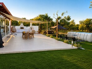 A patio with a table and chairs, a hanging chair, a barbecue area, and a swimming pool.