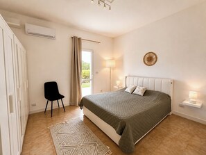 A bedroom with a bed, a chair, a bedside table, a lamp, and a wall-mounted air conditioner. - Apulian Villa with Outdoor Pool, AC & Olive Grove near beautiful Beaches (Puglia)