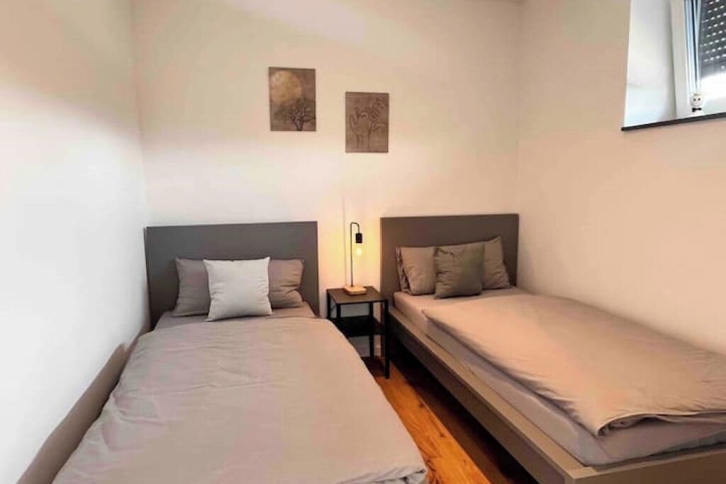 Una habitación pequeña con dos camas, una mesita de noche y una lámpara fijada a la pared.