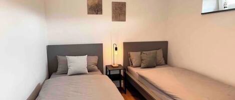 Una habitación pequeña con dos camas, una mesita de noche y una lámpara fijada a la pared.