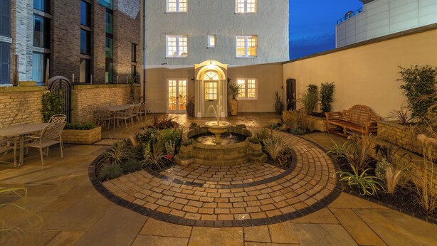 A courtyard with a fountain, outdoor seating, and a building with multiple windows.