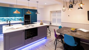 A modern kitchen with teal cabinets, a central island with a sink, and pendant lighting.
