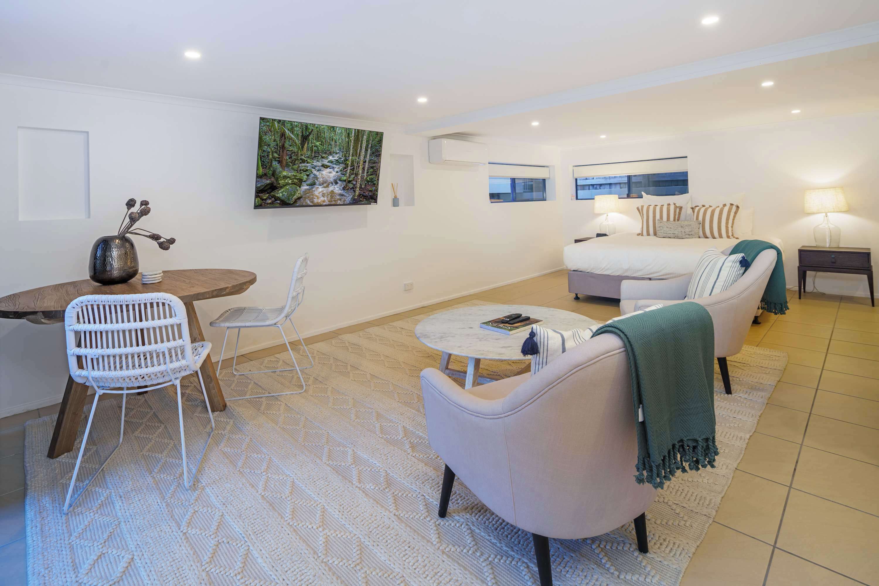 A modern living room with a sofa, chairs, a coffee table, a bed, and artwork on the walls.
