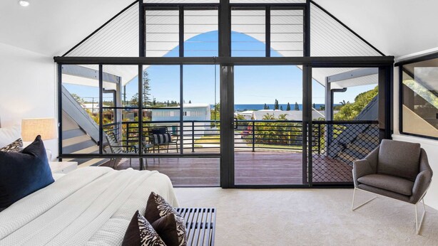 Et moderne soveværelse med en stor skydedør, der fører ud til en balkon med havudsigt.