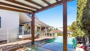 Et moderne hus med swimmingpool, en overdækket terrasse og udsigt til omkringliggende huse.