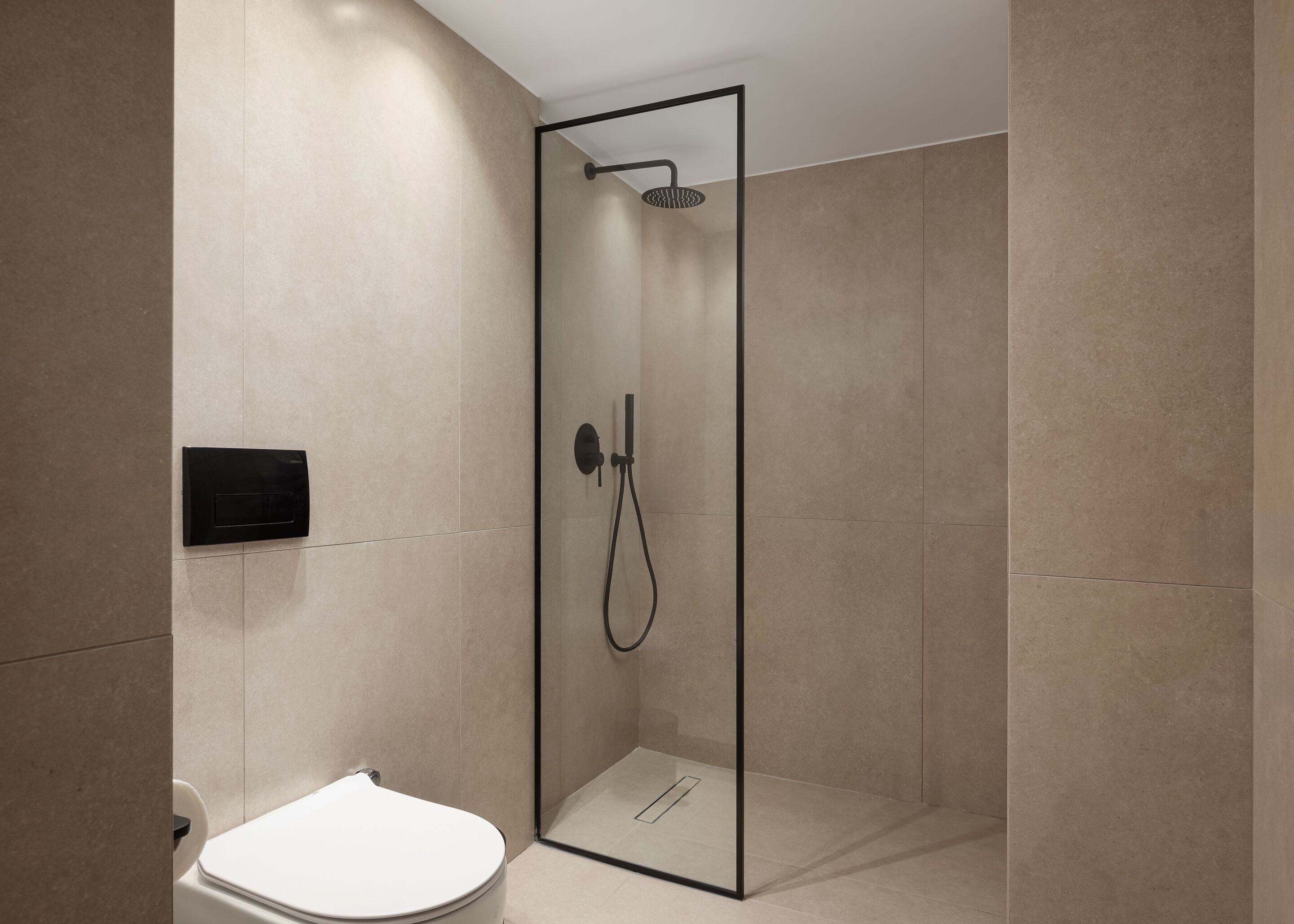 A modern bathroom with a glass-enclosed shower, a toilet, and a wall-mounted control panel.