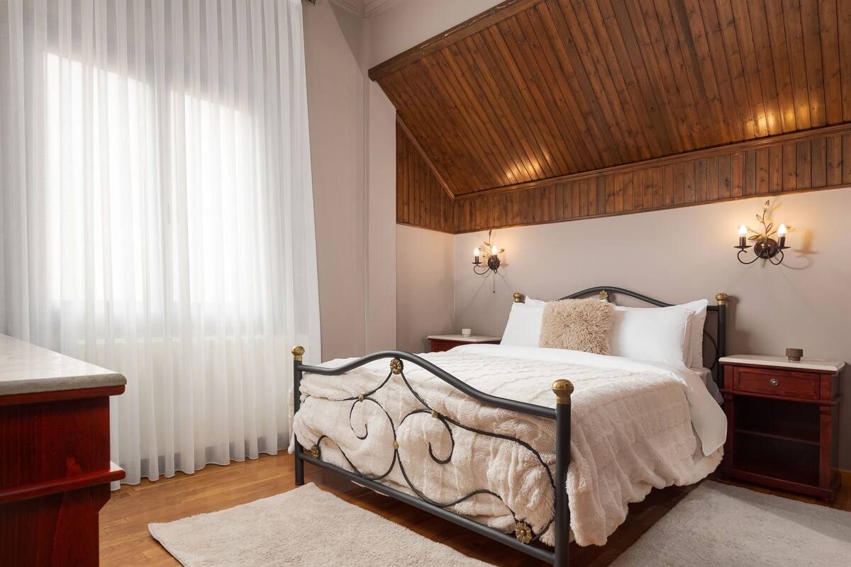 Une chambre avec un plafond en bois, un lit recouvert d’une couette blanche, deux tables de chevet et une petite table de nuit.