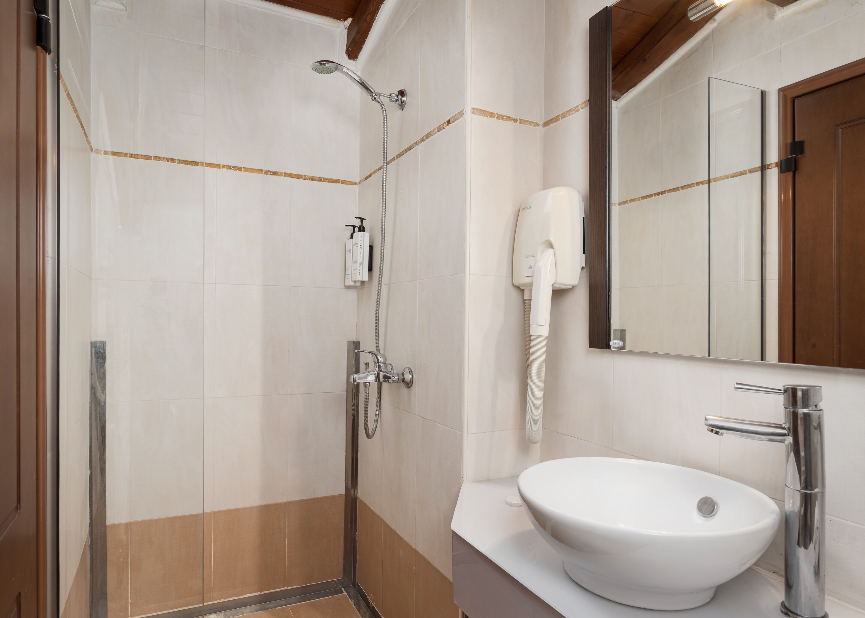 Un baño con cabina de ducha de vidrio, un lavamanos blanco y un secador de pelo fijado a la pared.