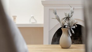 Ein Wohnzimmer mit Kamin, einem darüber hängenden Fernseher und einer Vase mit getrockneten Blumen auf einem Holztisch.