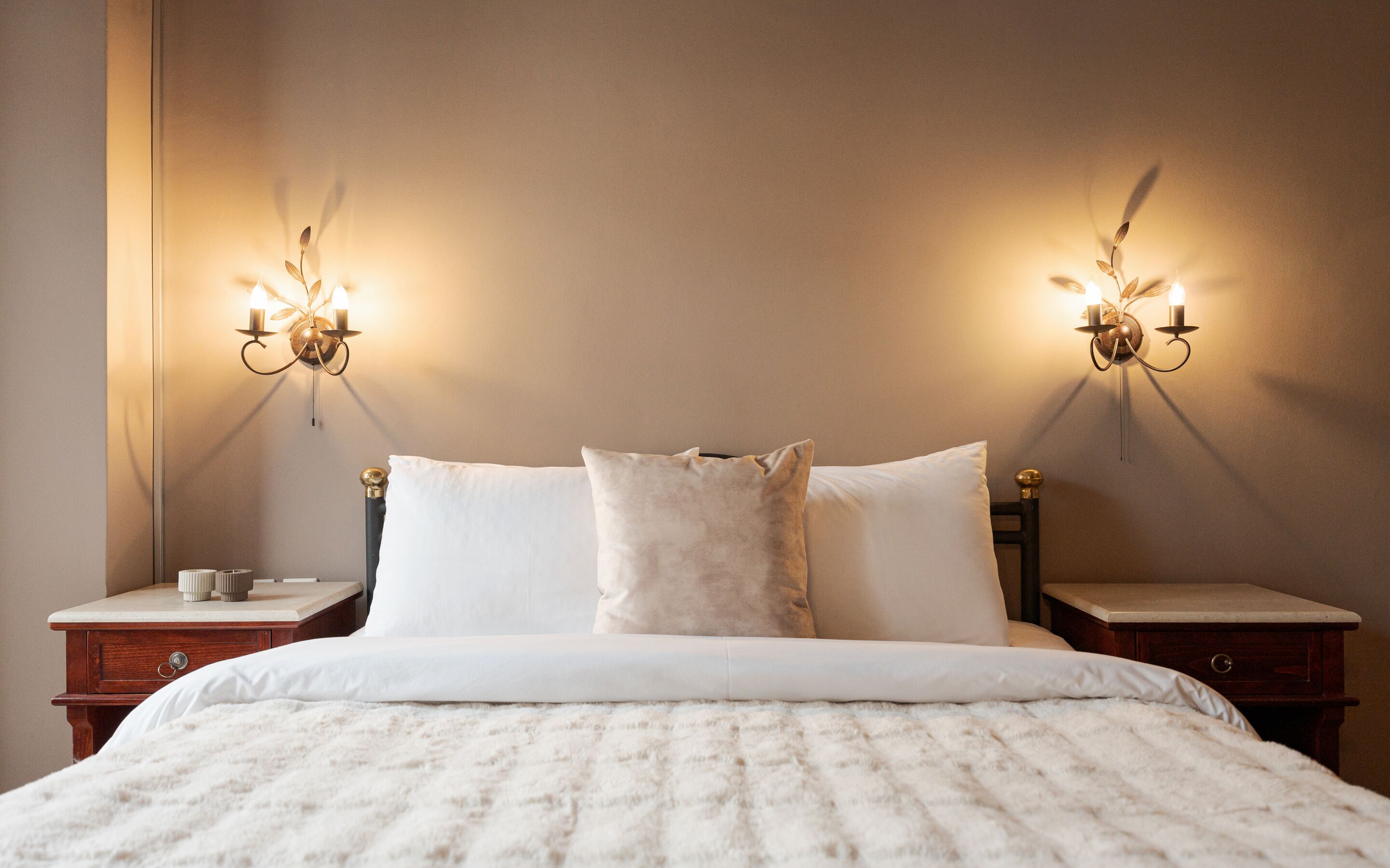 Una cama bien hecha con sábanas blancas y un edred ón blanco mullido, con dos mesitas de noche, cada una con una pequeña mesa y un candelabro.